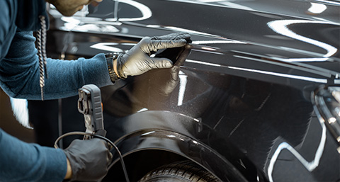 a man using a light to observe a car body for damage