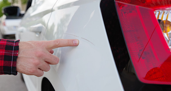 a person pointing at a vandal scratch on a white car