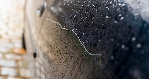 a vandal scratch on the site of a black car wet from the rain