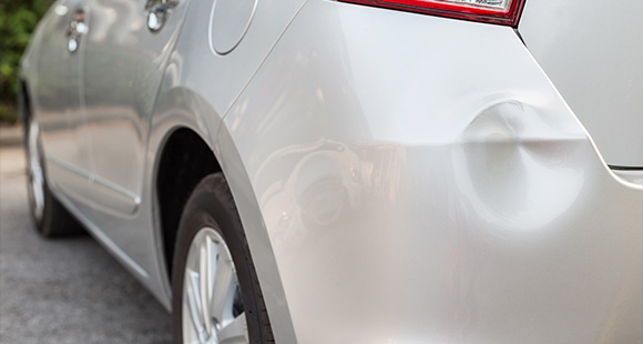 a dented area on the back of a silver car from a minor collision