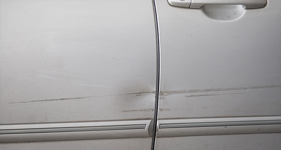 the side of a silver car with a dent and scratch going across the rear door to the driver door