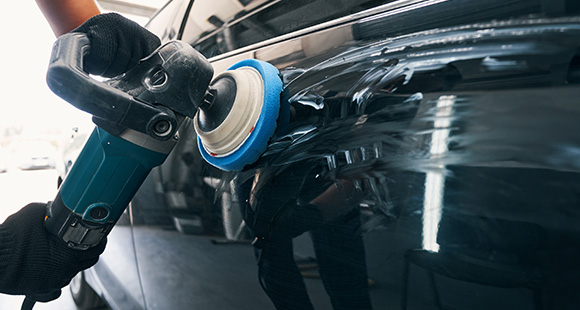 a person using a handheld machine polisher to buff the body of a black car