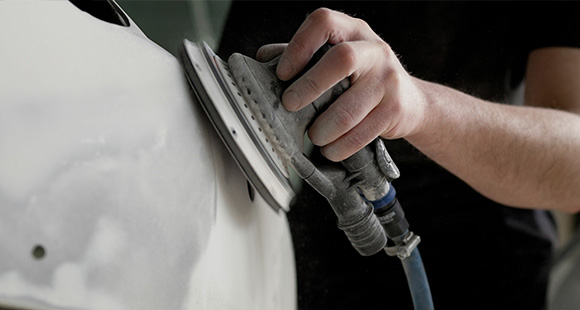 a person using a handheld grinder to prepare the bumper of a car for painting